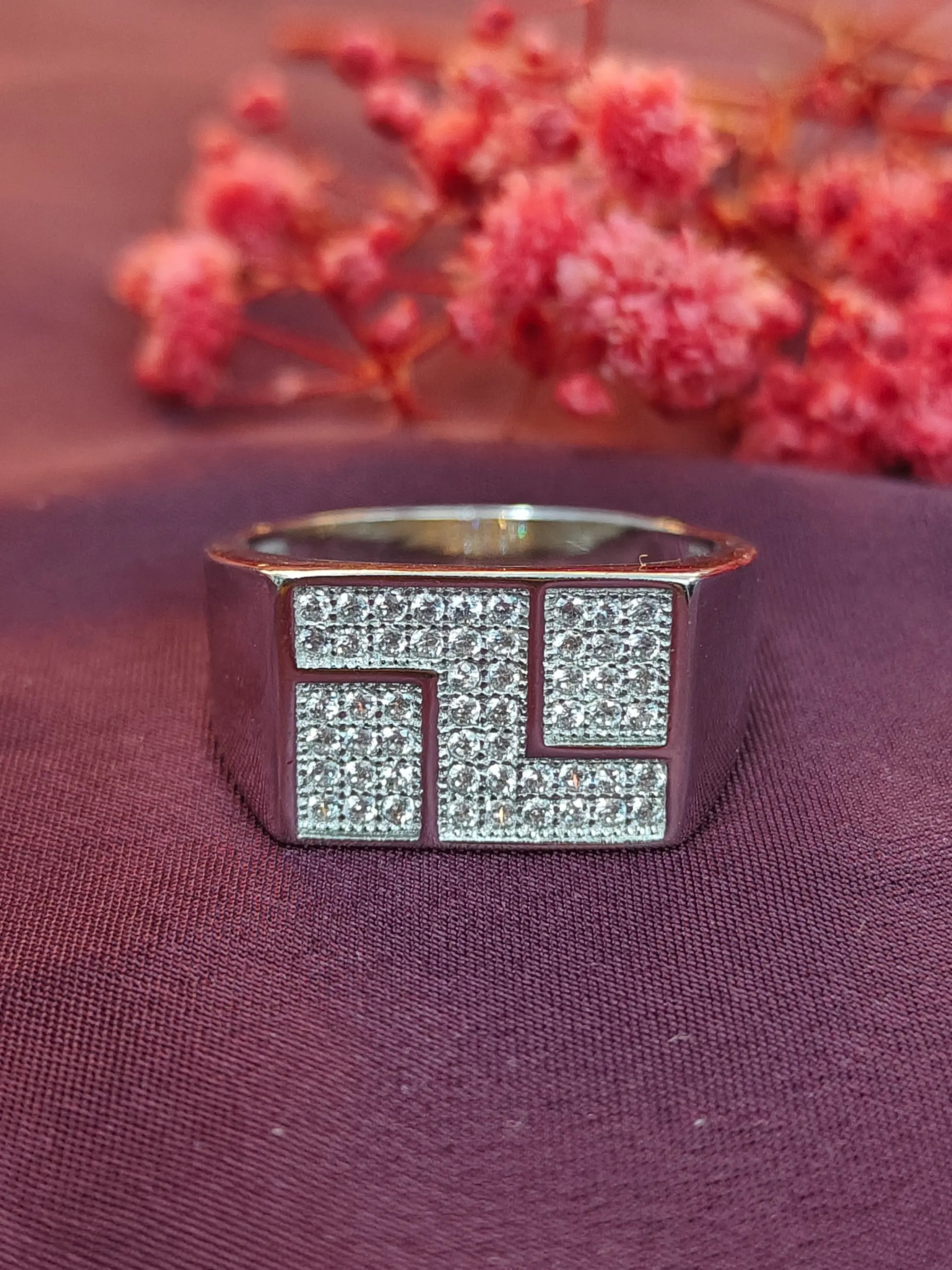 Silver ring with a geometric design on a purple fabric background with pink flowers.
